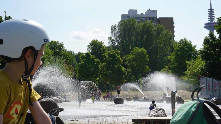 Kind im Vordergrund schaut den Kindern bei den Wasserspielen im Niddapark Frankfurt zu