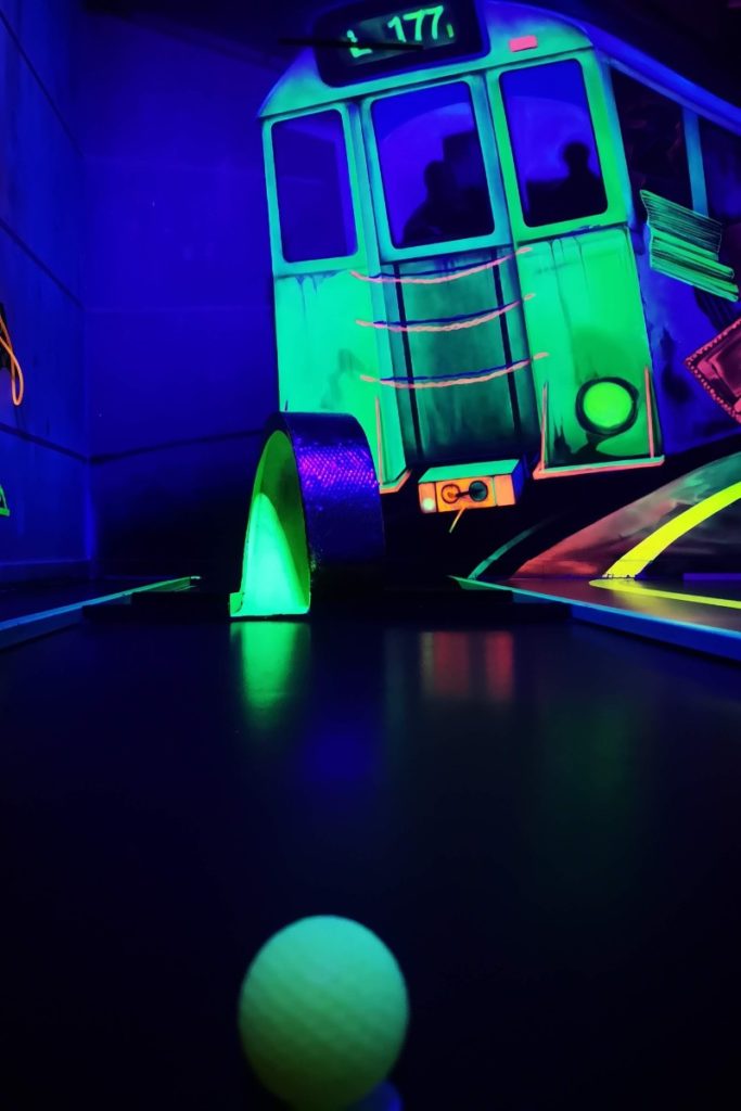 Ein Ball im Fokus bei der Minigolfbahn bei den Schwarzlichthelden, im Hintergrund Graffiti und eine Spirale, durch die der Ball gehen muss